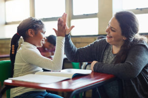 Shot of a young girl giving her teacher a high five in a classroom